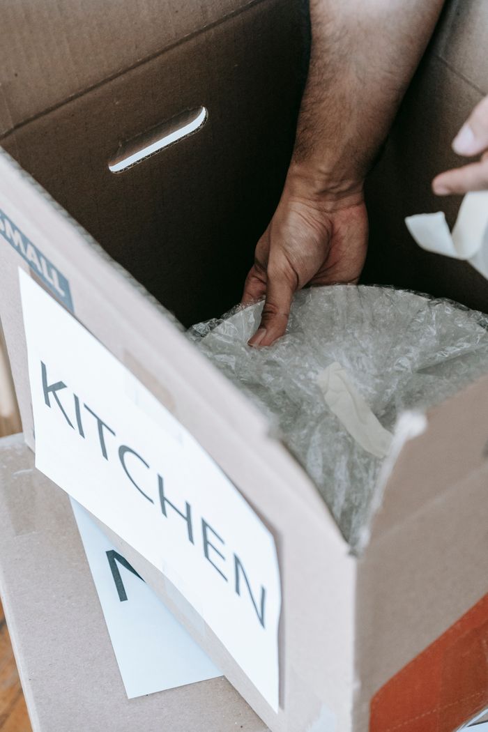 Vue rapprochée d’objets de cuisine emballés pour un déménagement dans un carton étiqueté, à l’intérieur.